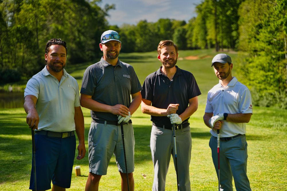 Group of four golfers posing together on fairway with trees in background.