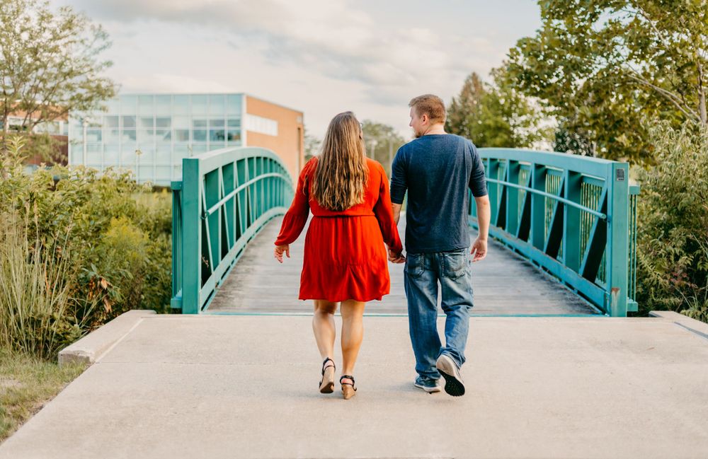 A couple walking hand in hand on a turquoise bridge in casual attire.