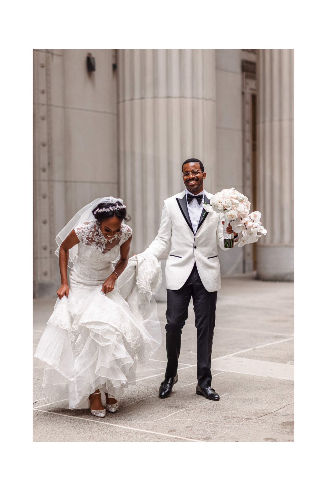 A joyful wedding couple share a candid moment between classical columns.