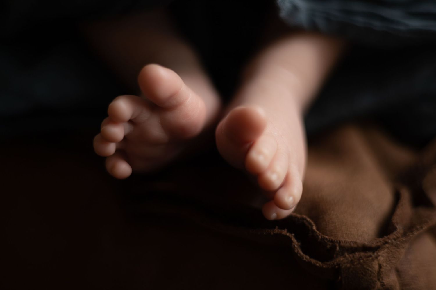 Close-up of tiny baby toes against dark background with dramatic lighting.