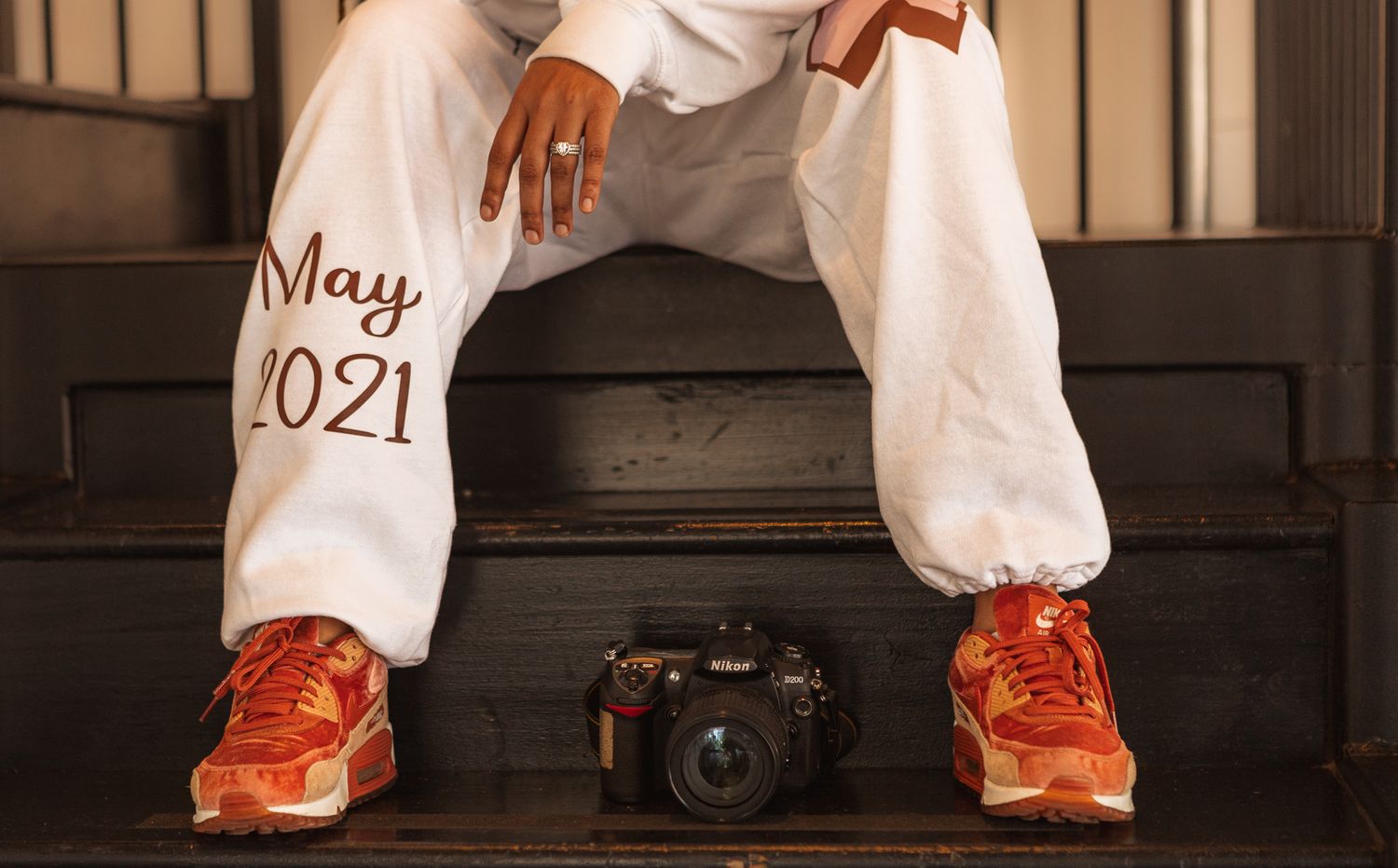 Orange sneakers and white pants with 'May 2021' text visible next to a camera on dark floor.