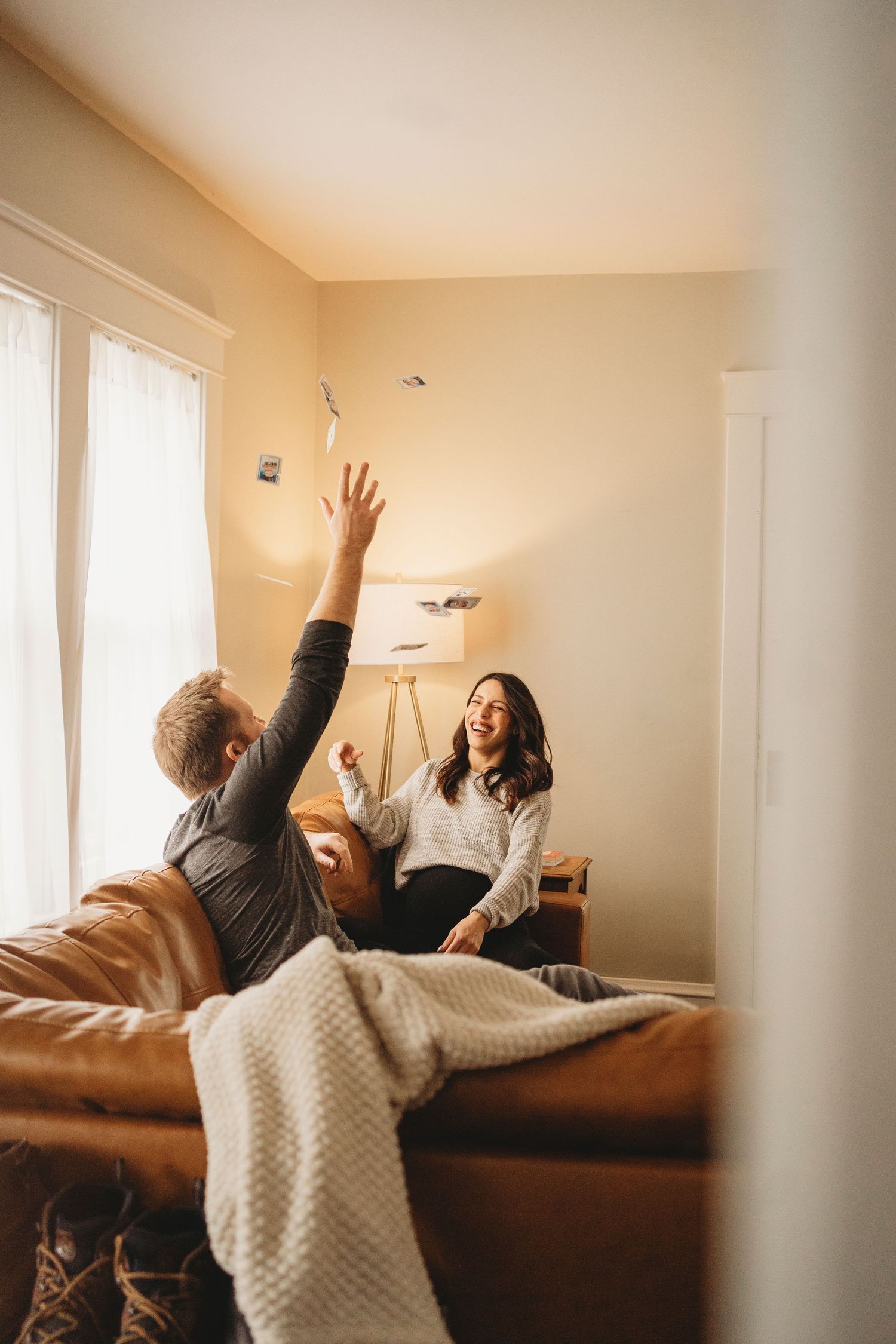A playful moment captured as people toss papers in the air on a leather couch.