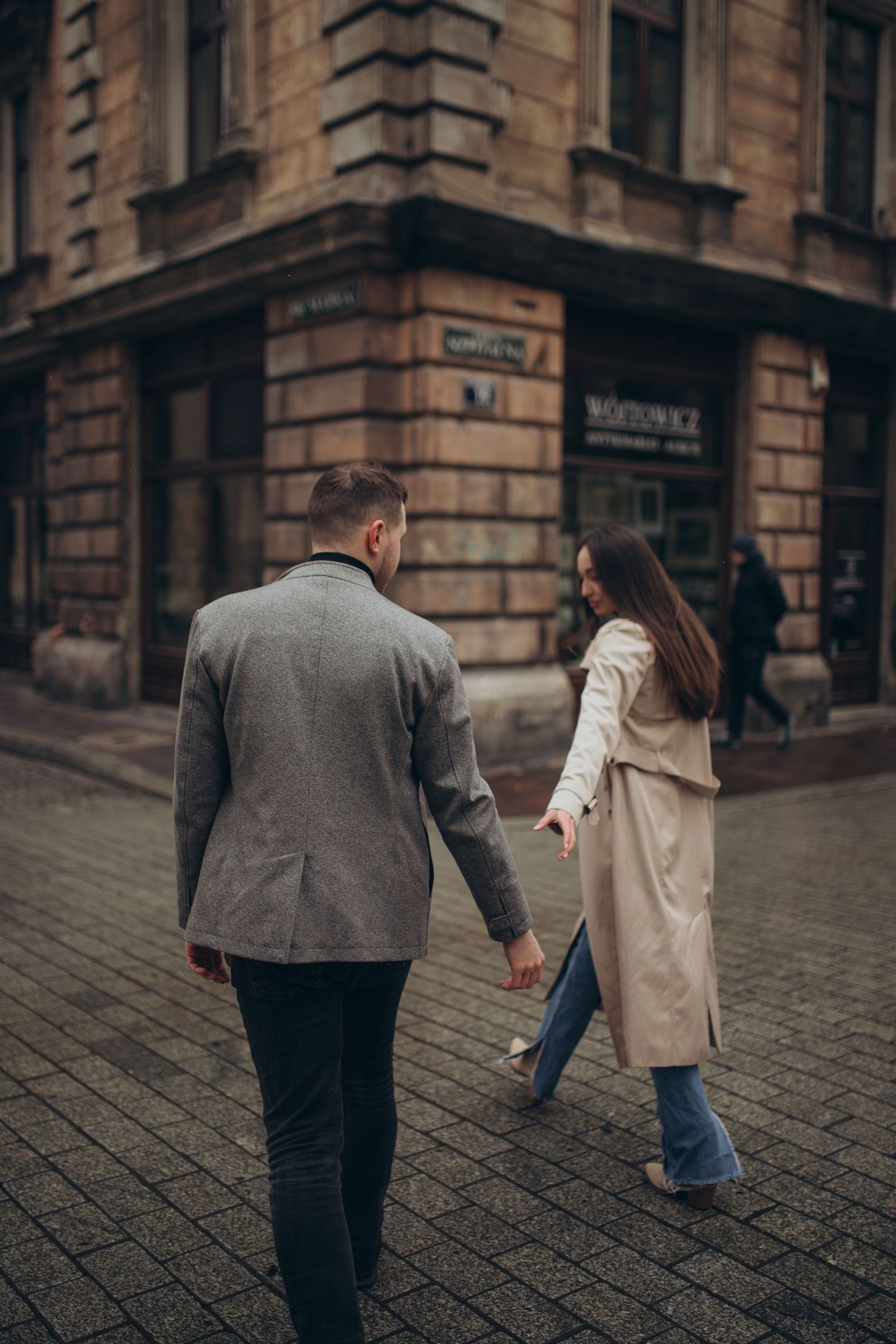 Couple walking on cobblestone street near historic building corner in urban setting.