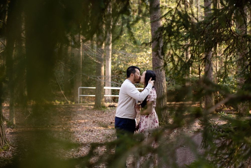 A romantic couple shares an intimate moment while embracing in a sunlit forest setting.