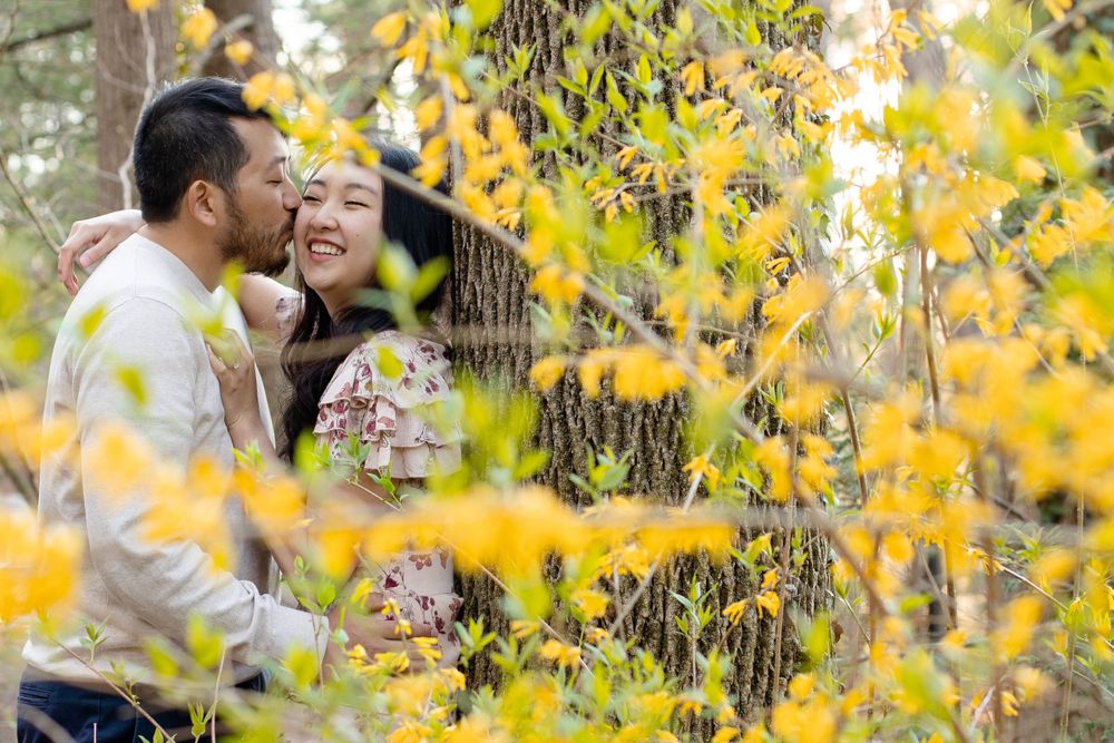A romantic autumn moment captured through yellow leaves as a couple embraces in a forest setting.