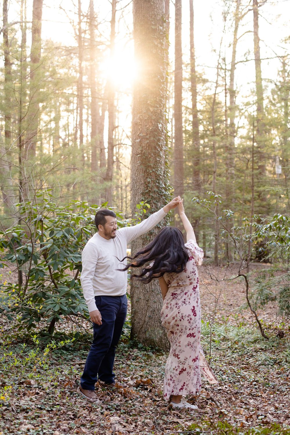 A couple dances playfully in a sunlit forest clearing surrounded by spring foliage.