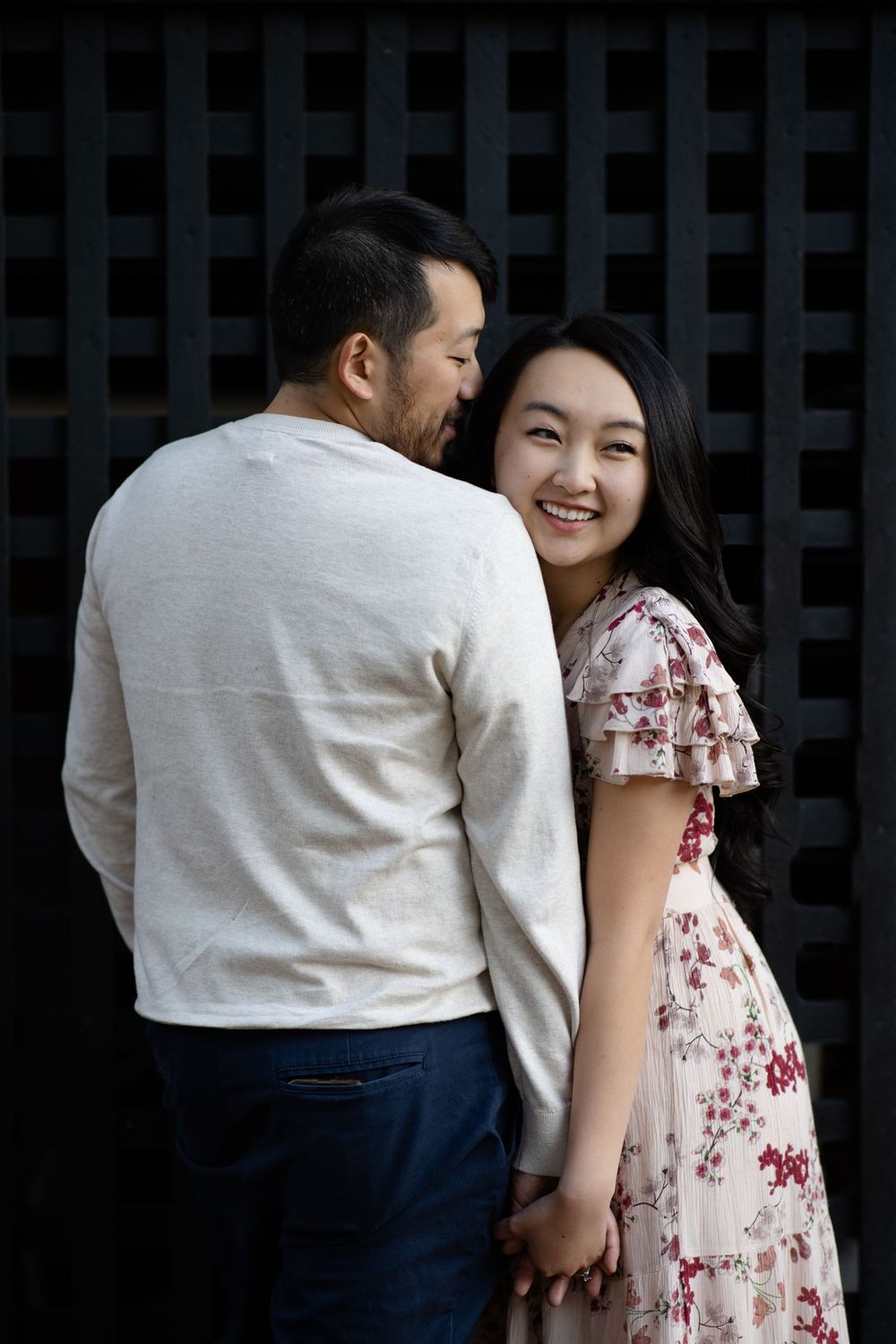 A tender moment between a couple in formal wear against a dark latticed background.