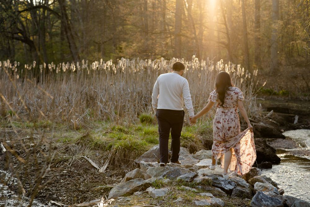 A couple holds hands while walking along rocky riverbank during golden hour.