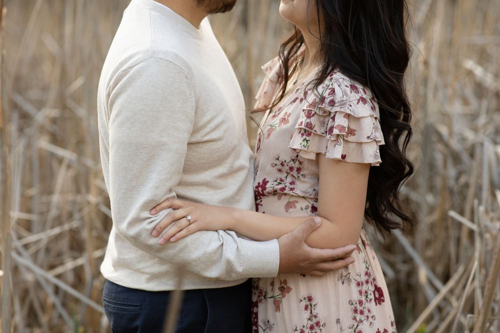 A close-up of a couple embracing among dried cattails in soft natural light.