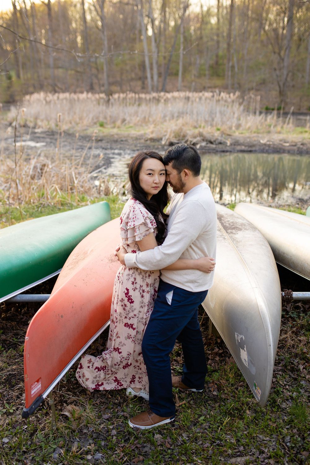 Romantic moment between couple standing among colorful canoes by a serene lake.