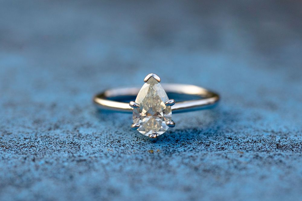 Pear-shaped diamond engagement ring on blue textured background.