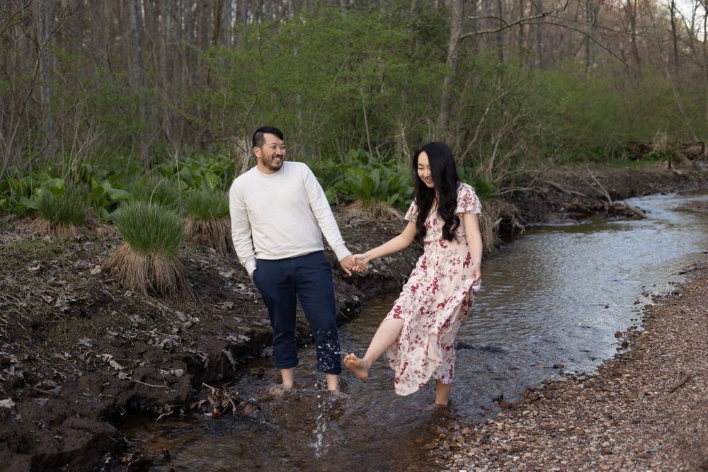 Couple holding hands while standing in a creek bed surrounded by nature.