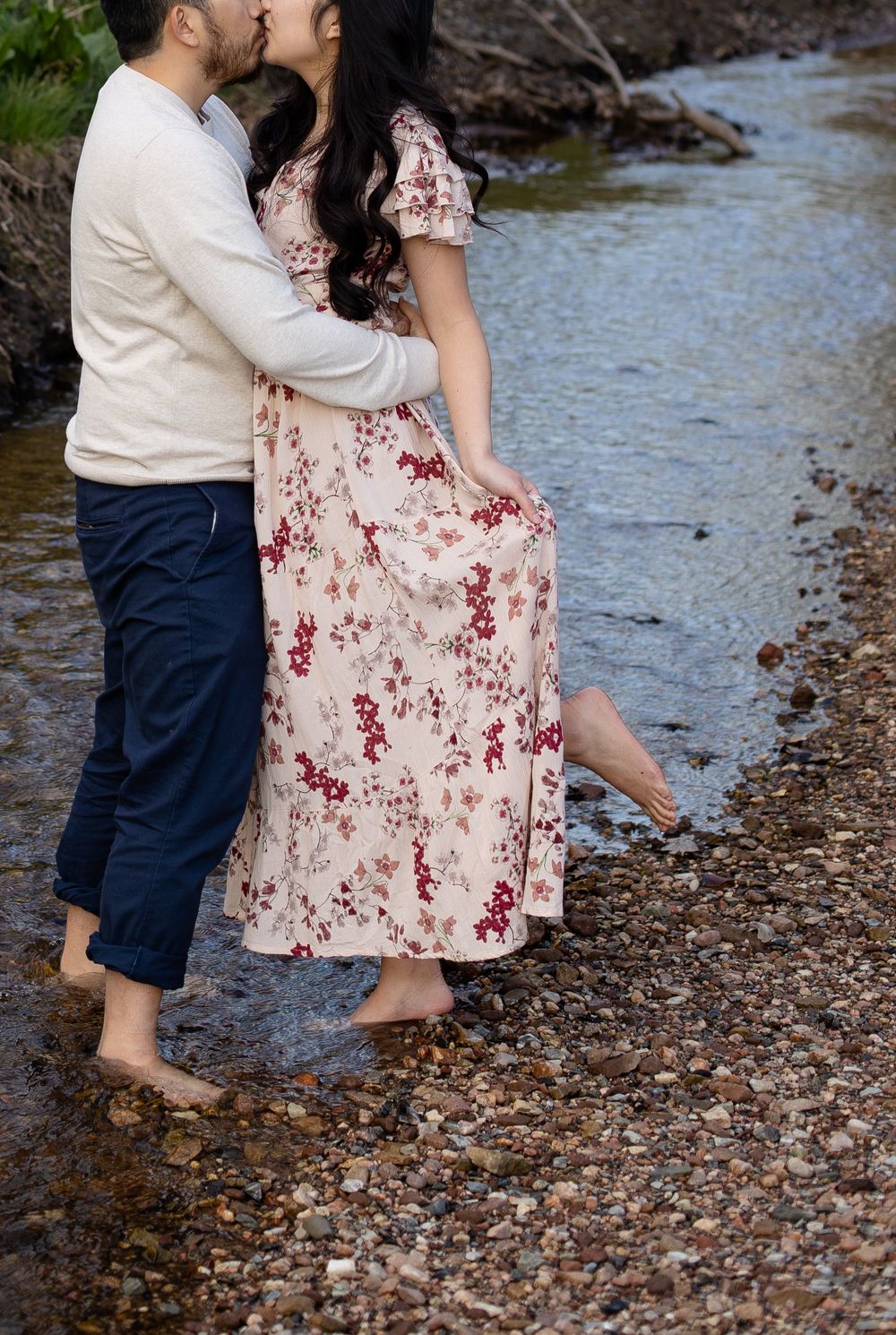 Couple standing barefoot in creek waters wearing coordinated casual outfits.