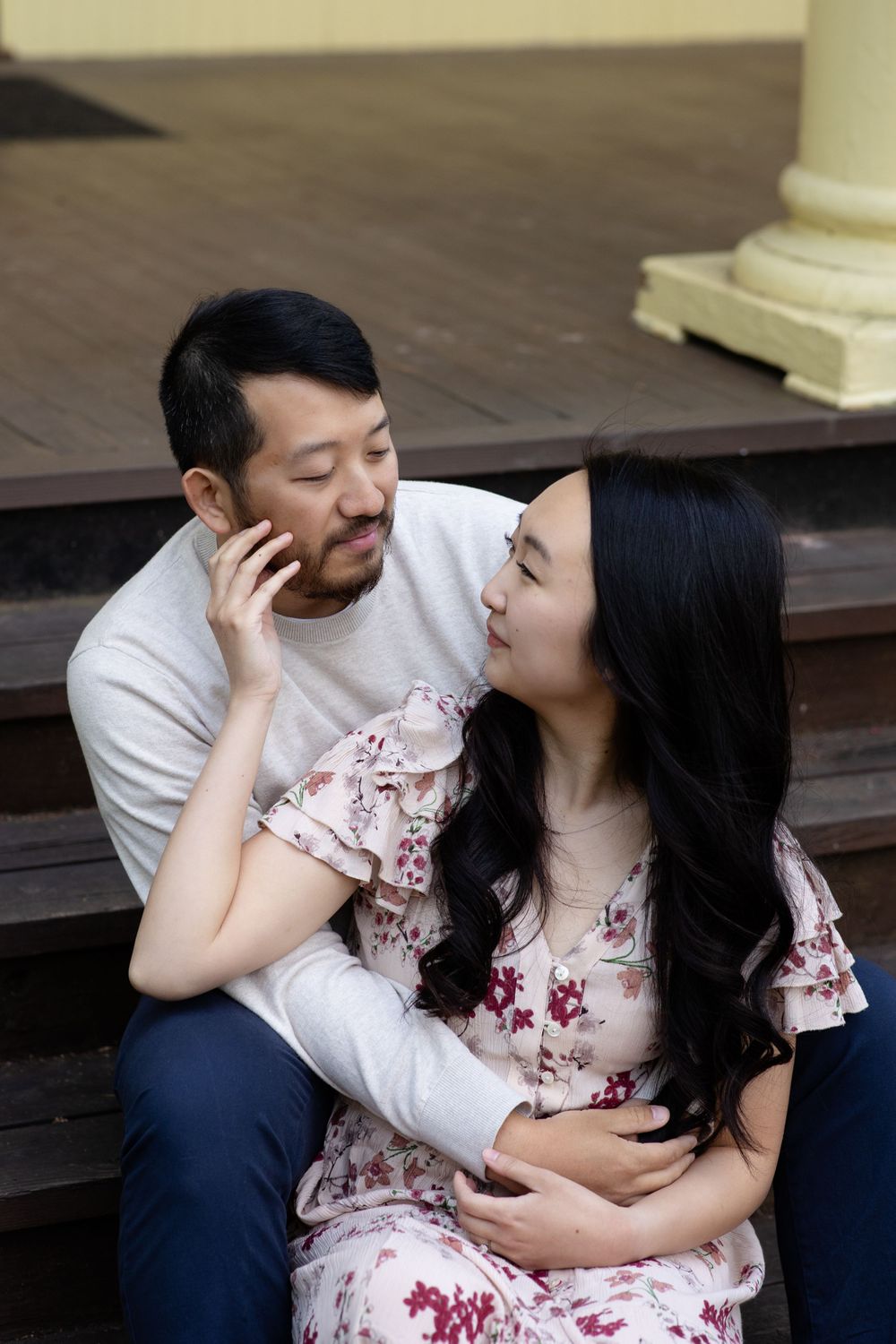 A couple shares a tender moment while sitting on outdoor steps near a decorative column.