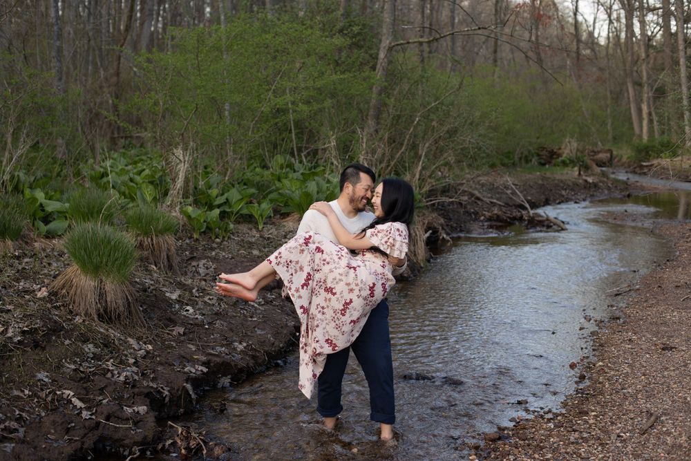 Playful couple moment captured by a creek in a wooded setting.