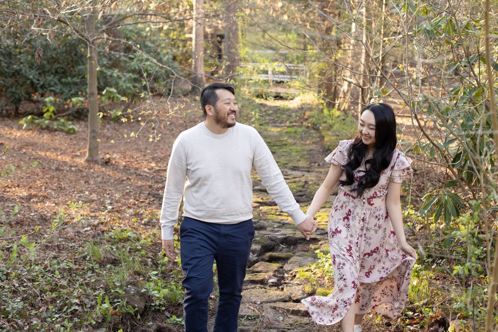 A couple holds hands while walking along a scenic forest trail.