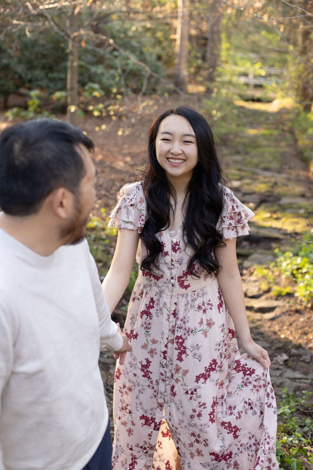 A couple shares joyful expressions while standing on a woodland path.