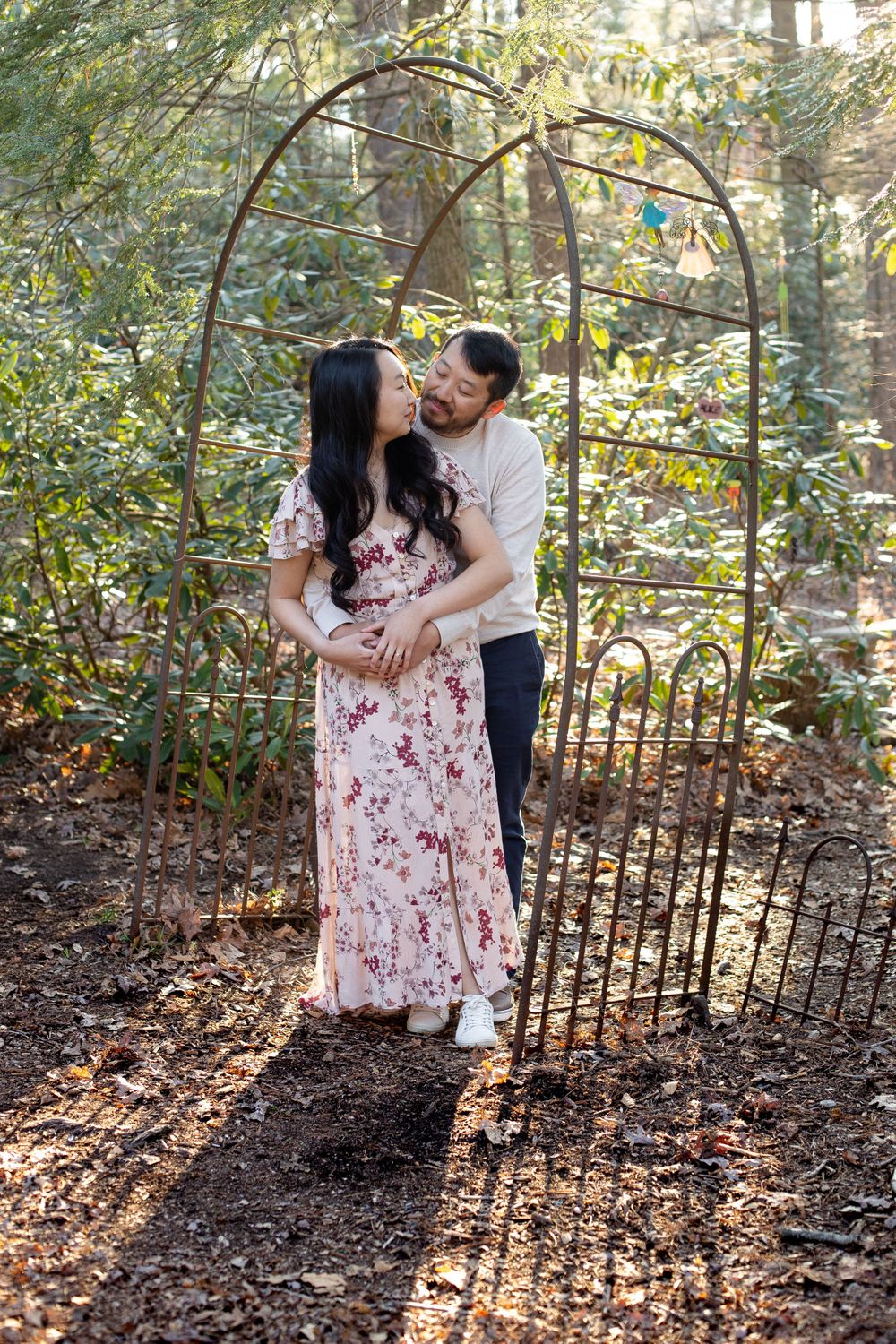 A couple shares an intimate moment by a decorative garden arch in dappled sunlight.