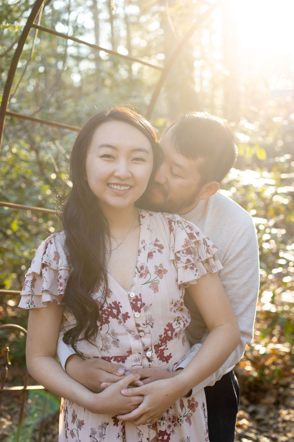 A couple embraces in golden sunlight filtering through trees during a romantic photoshoot.