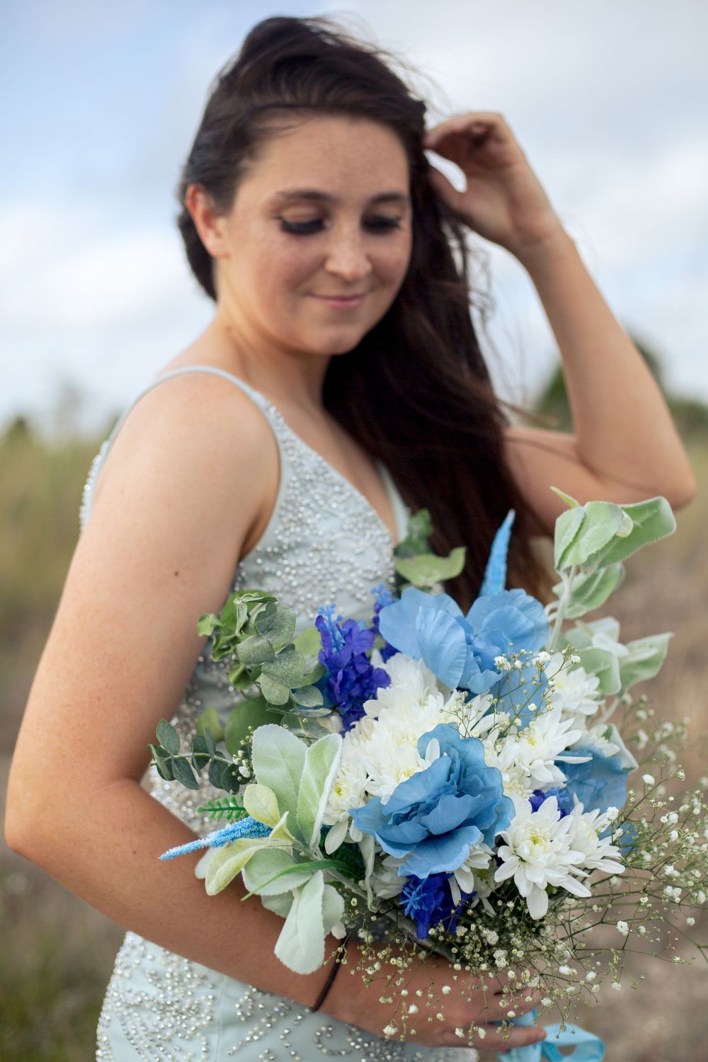 Beautiful bridal portrait with blue and white floral arrangement against natural background.