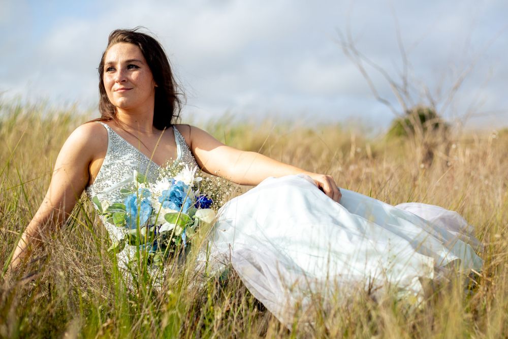 A bride in a beaded dress with blue bouquet poses gracefully in golden wheat field.
