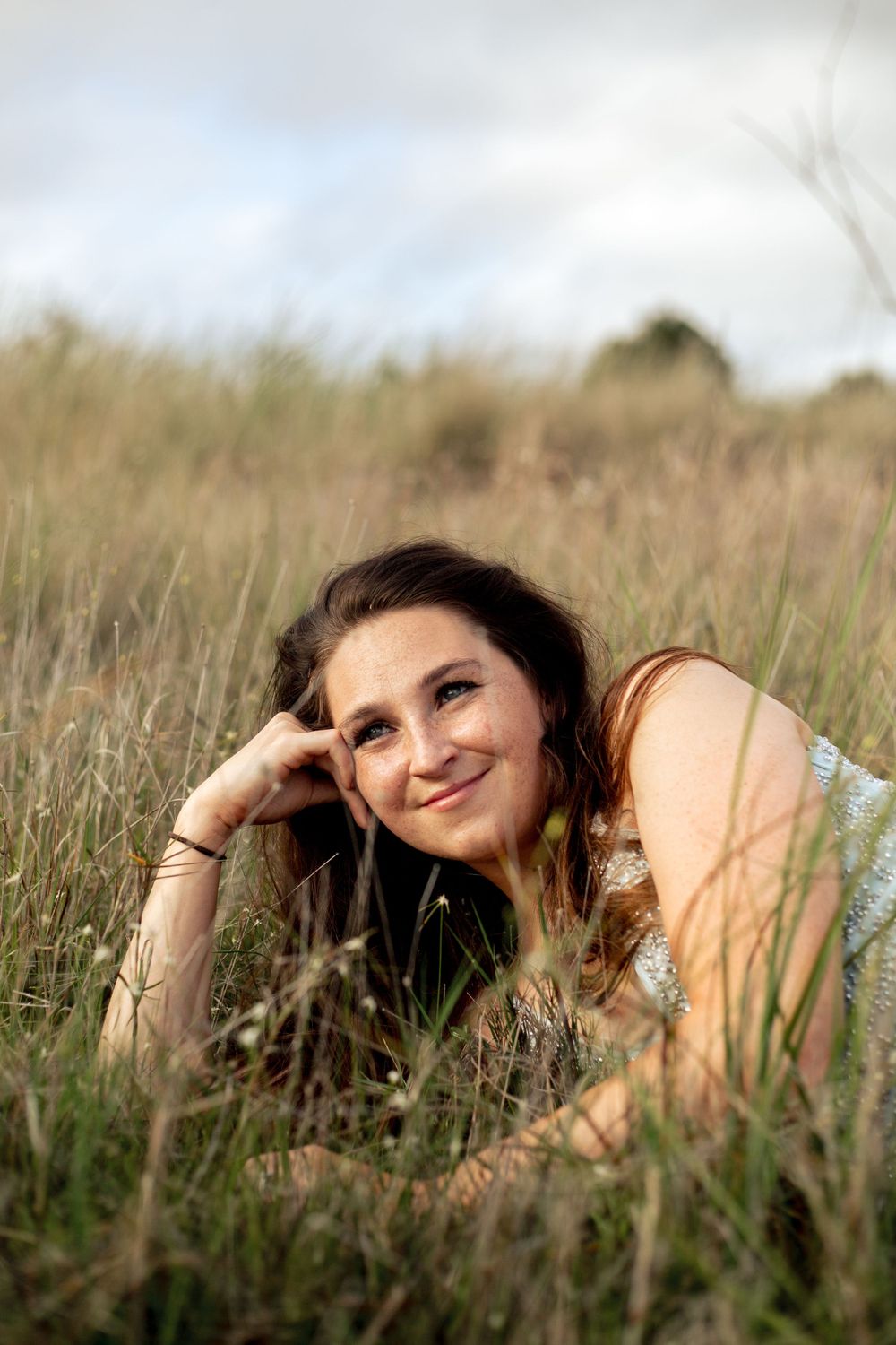 Bride resting in tall grass field during golden hour portrait session.