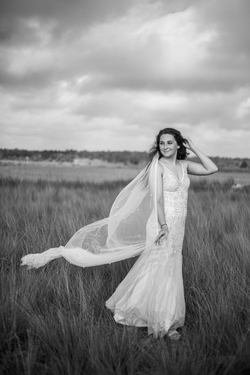 Dramatic black and white photo of bride with flowing veil in marsh grass.