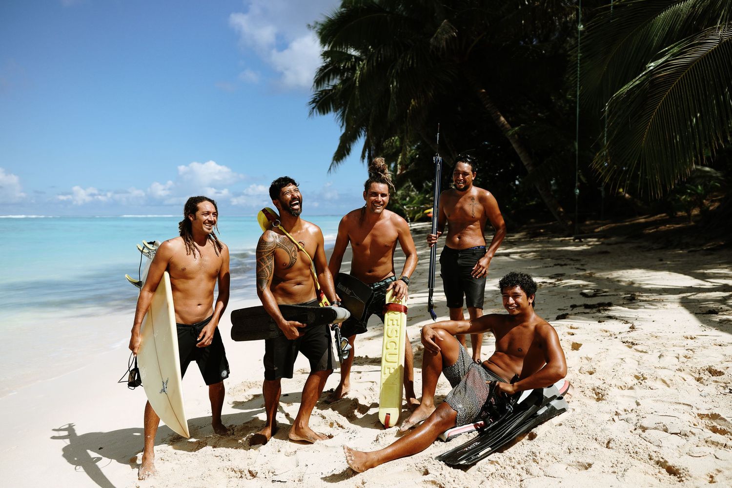 Surfers with their boards posing together on a palm-lined beach.