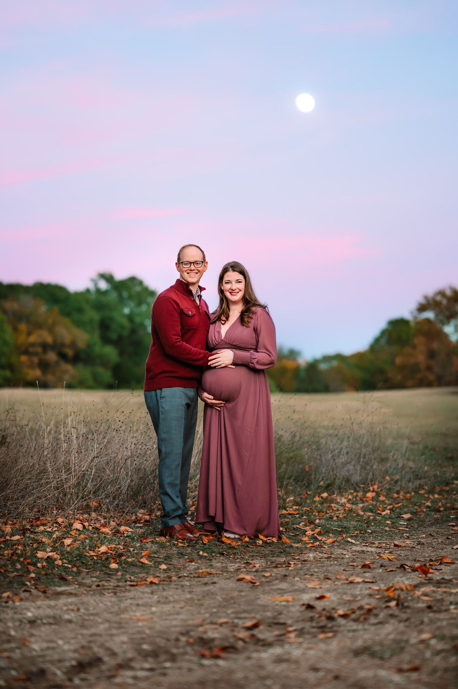 Mom and Dad smiling holding baby bump during outdoor Dallas area maternity photo session at sunset