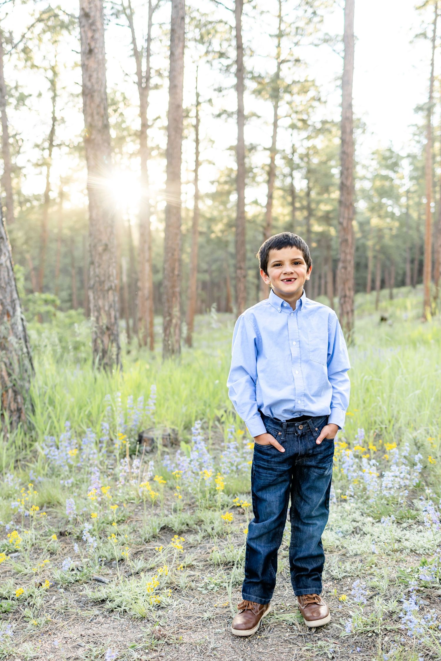 Young boy poses with hands in pockets and smiles at sunset during their family session in Colorado Springs.