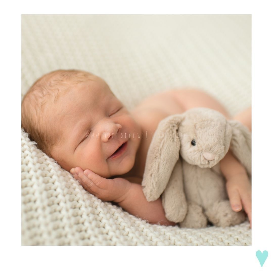 Sleeping baby cuddled with soft plush bunny toy on white knit blanket.