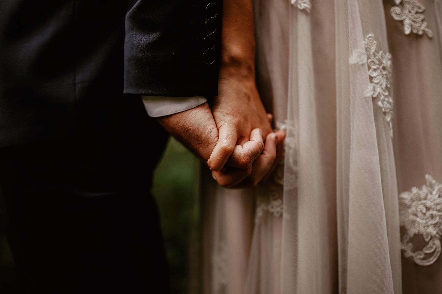Close-up shot of couple holding hands showing wedding attire details.