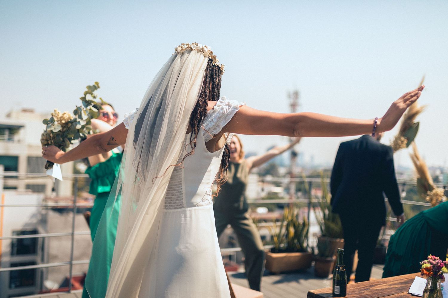 Bridesmaids in emerald green dresses celebrating on urban rooftop.