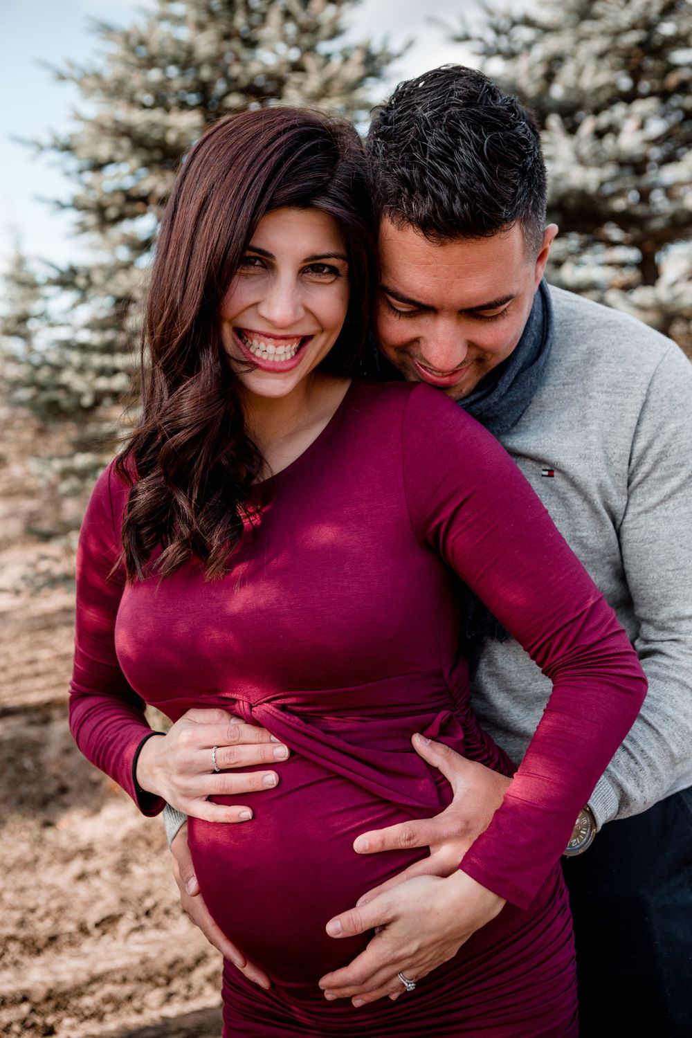 A couple shares tender moments during their outdoor maternity photoshoot among evergreen trees.