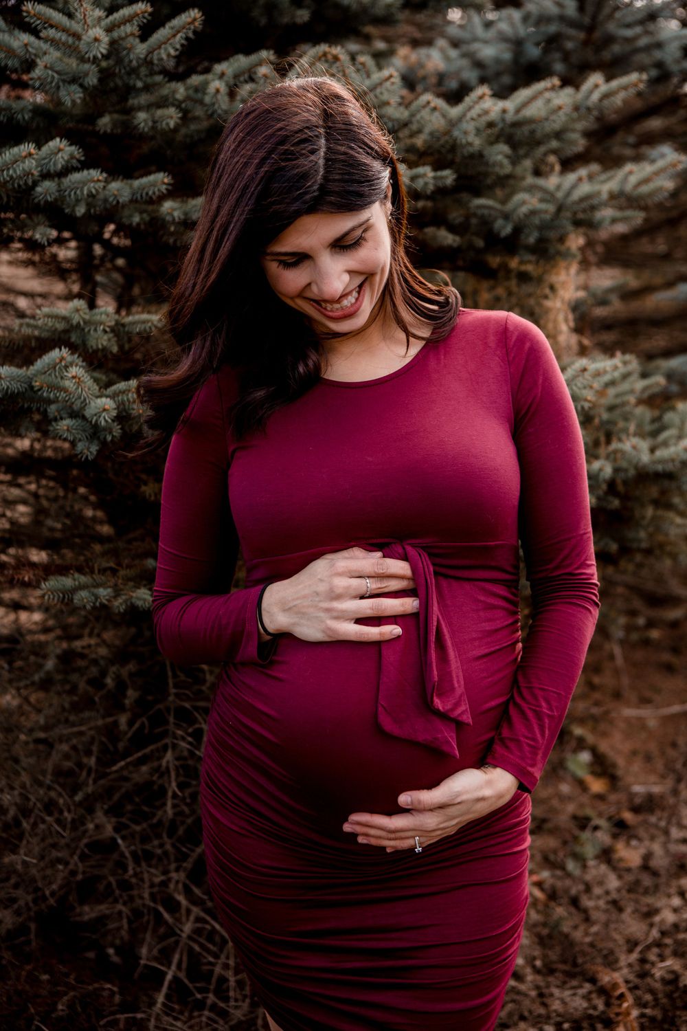 Close-up shots showcasing a pregnancy belly in a deep burgundy dress with gentle hands caressing.