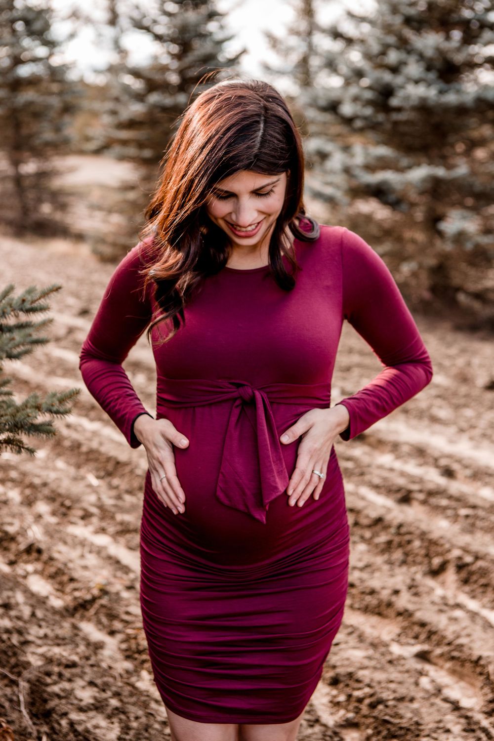 Maternity portraits in burgundy dress against snowy winter landscape.