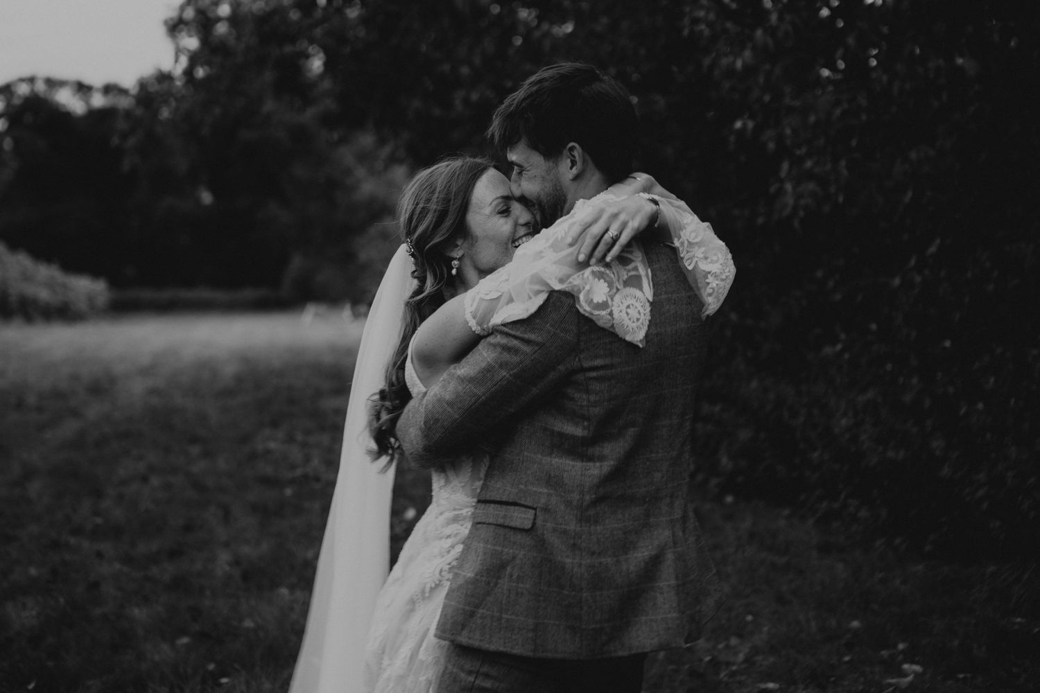 A tender black and white wedding photo showing an intimate embrace outdoors.