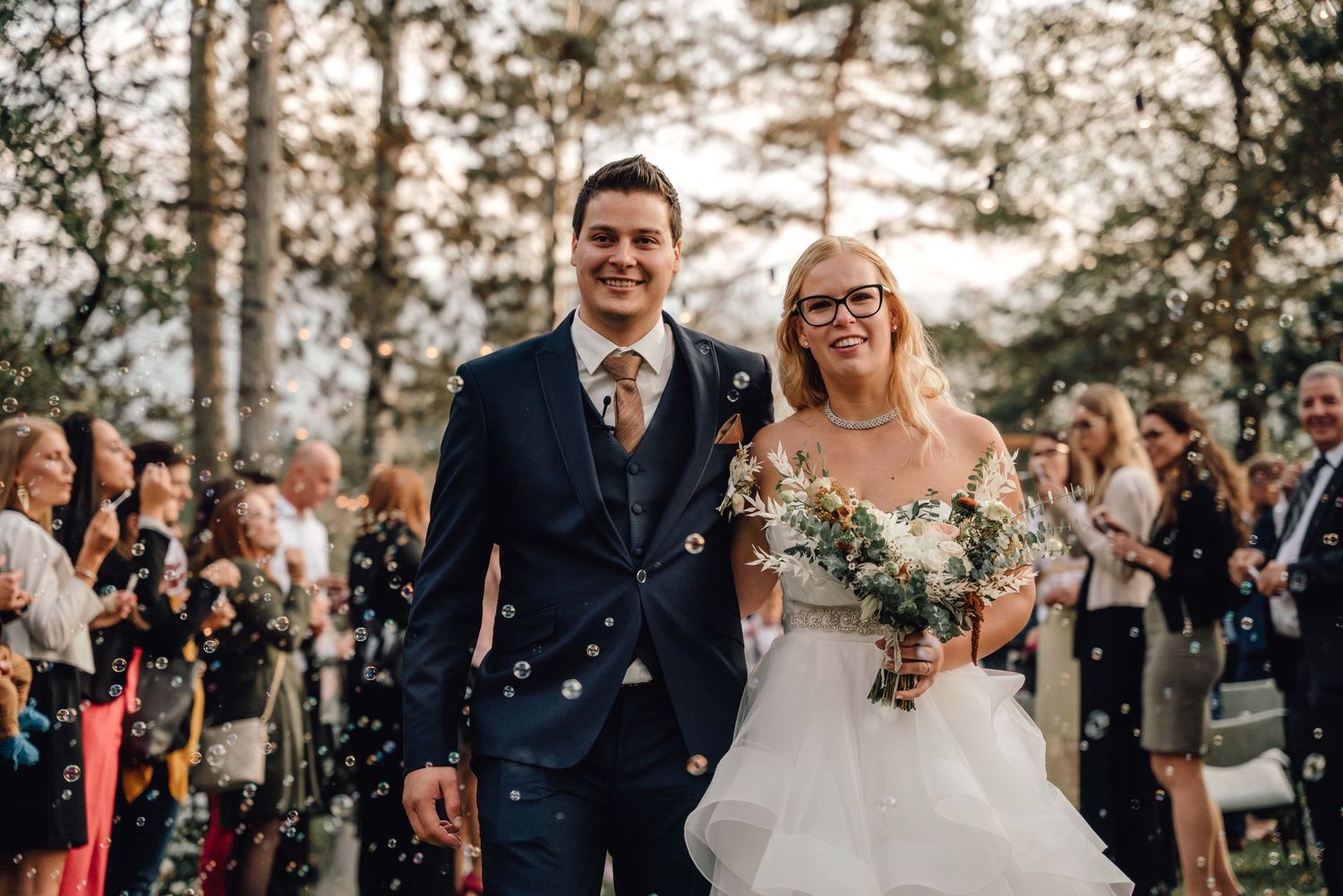 Joyful celebration with confetti at an outdoor wedding ceremony among pine trees.