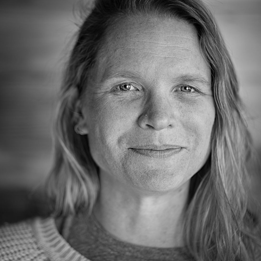 Black and white portrait of person with long hair and gentle smile wearing knit sweater.