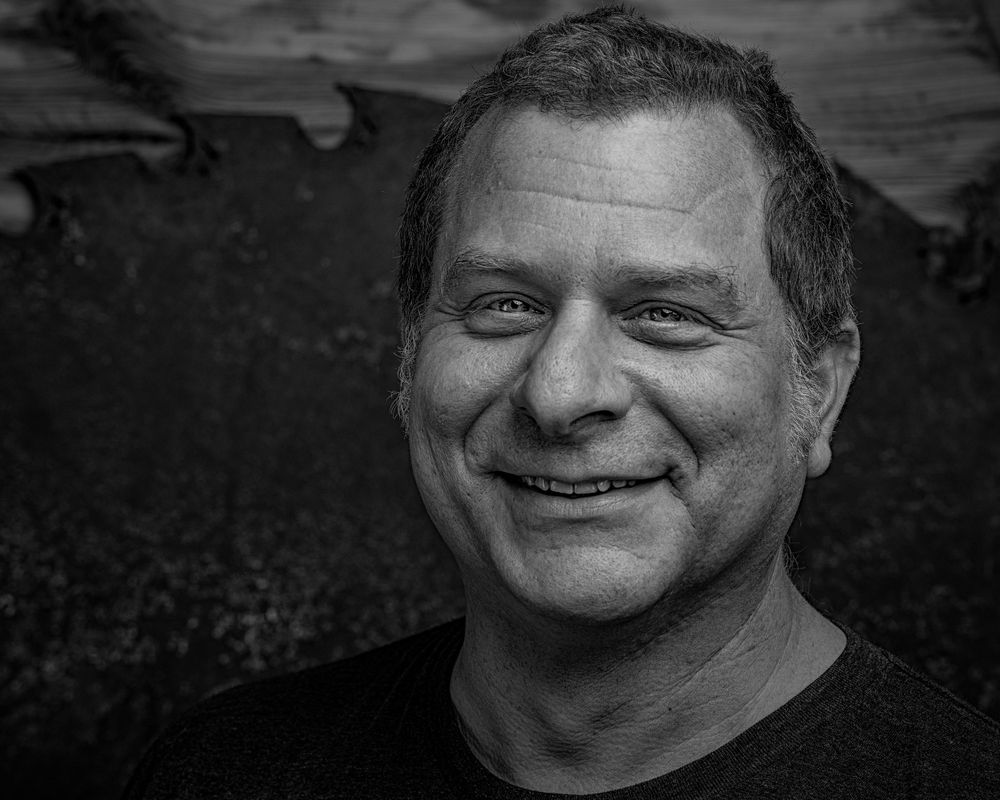 Black and white outdoor portrait showing warm genuine smile against natural landscape.