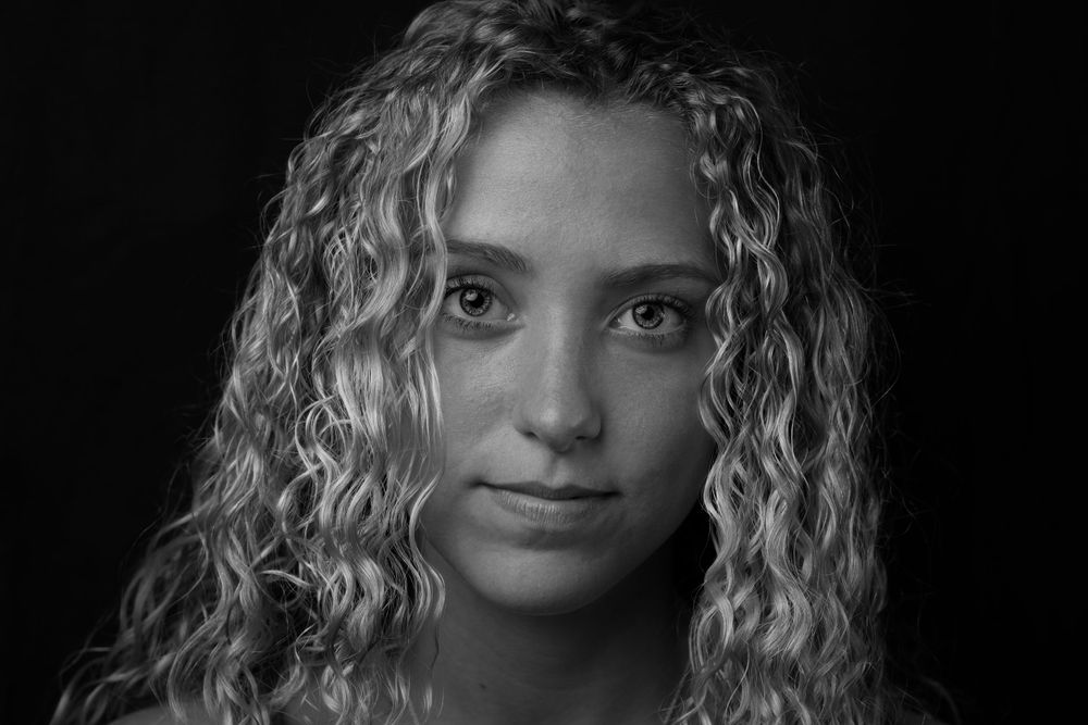 Dramatic black and white portrait featuring naturally curly hair and intense gaze.