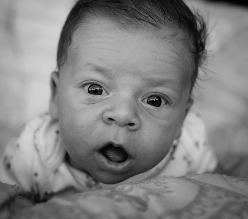 Close-up black and white portrait of wide-eyed infant with surprised expression.