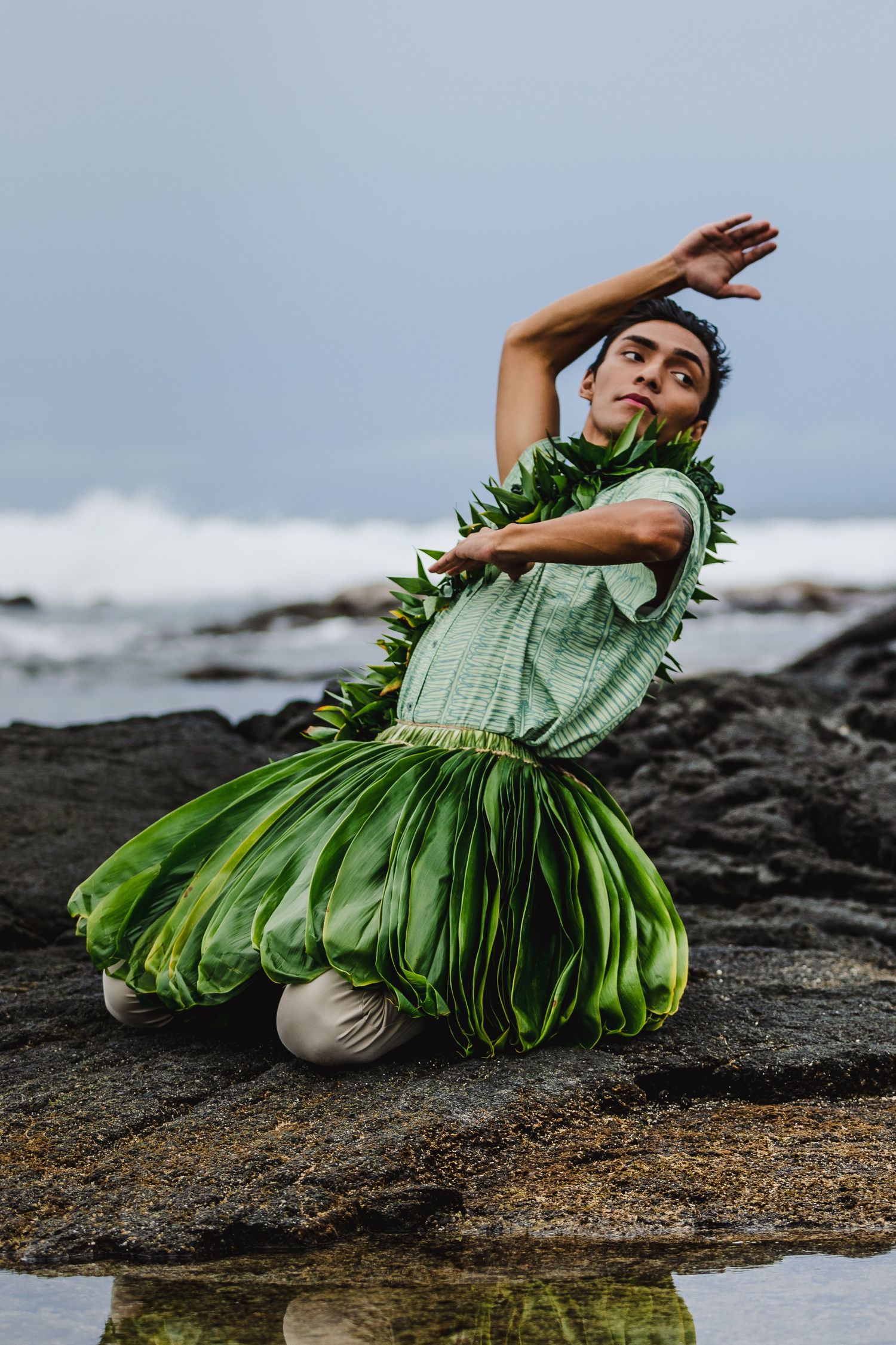 A traditional Hawaiian dancer performs on black lava rocks by the ocean.