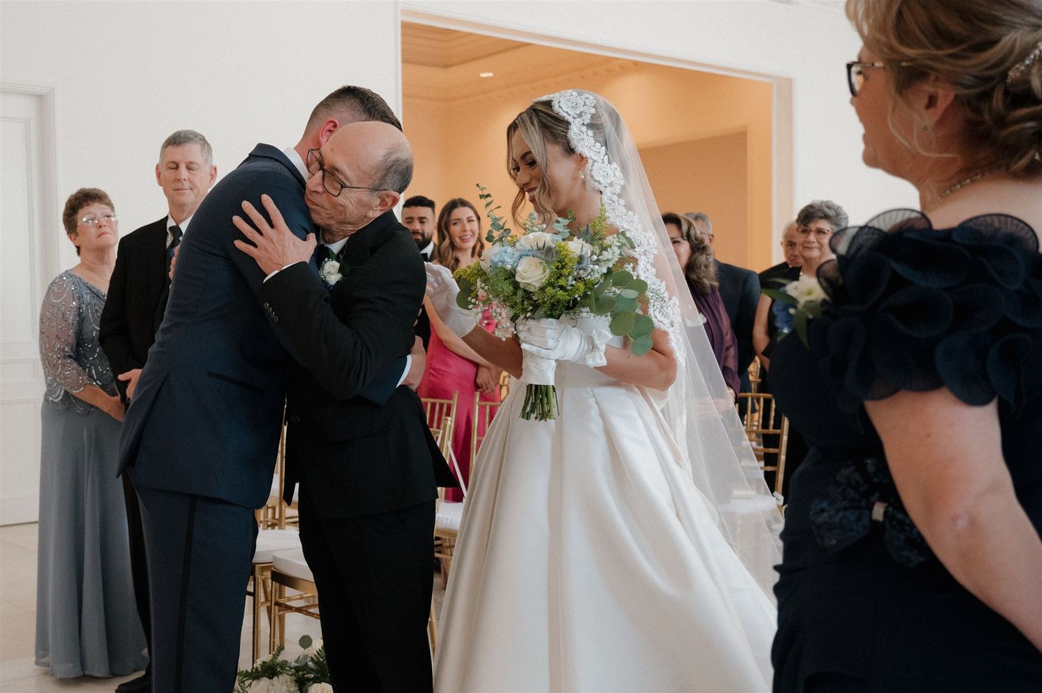 An emotional moment during a wedding ceremony as the groom wipes tears while the bride holds a lush bouquet.