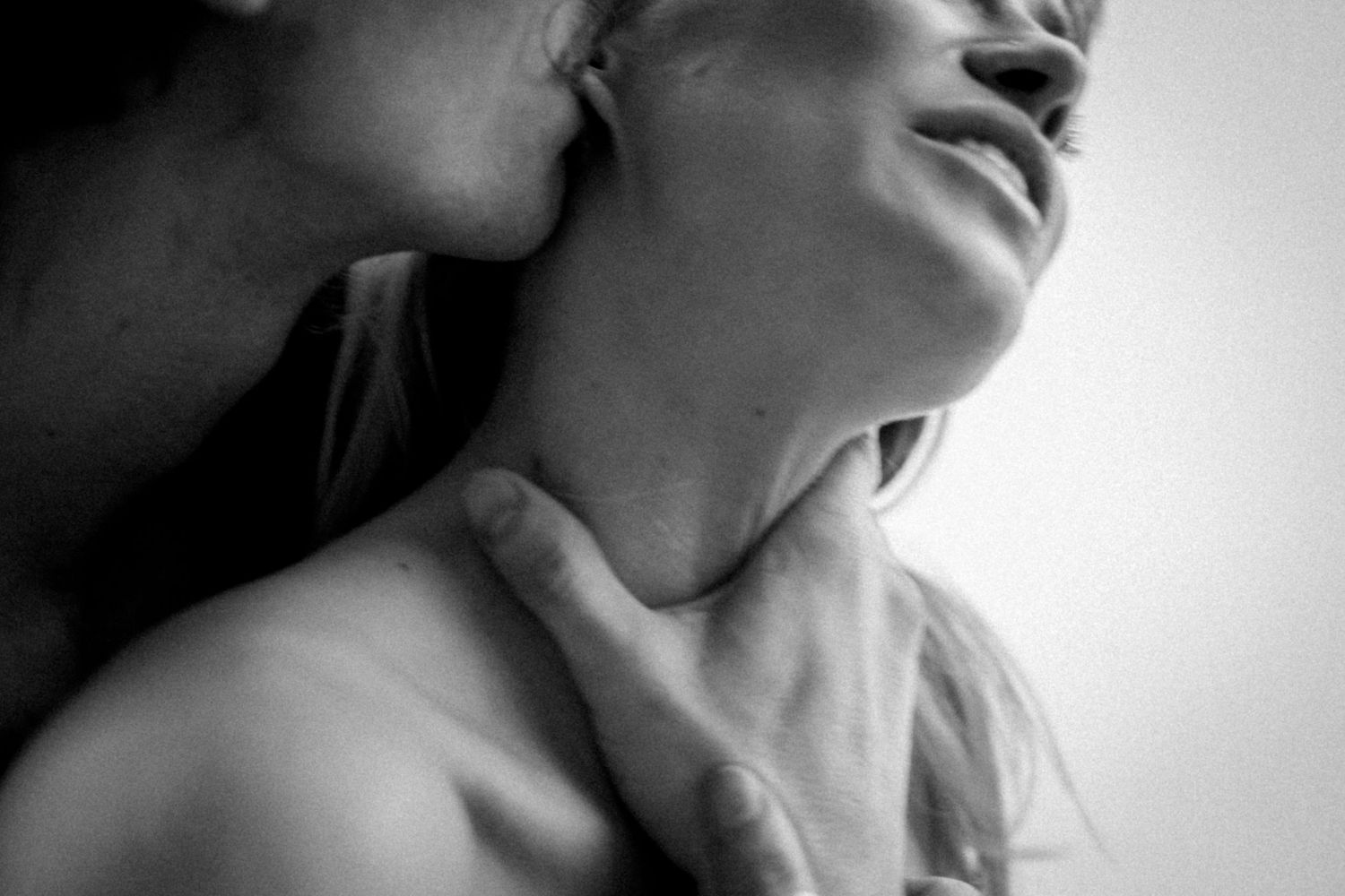Intimate black and white portrait showing neck and shoulder in soft lighting.