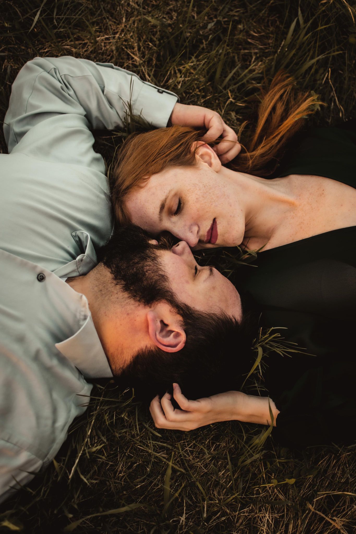 Intimate overhead shot of a couple lying together on grass in matching outfits.