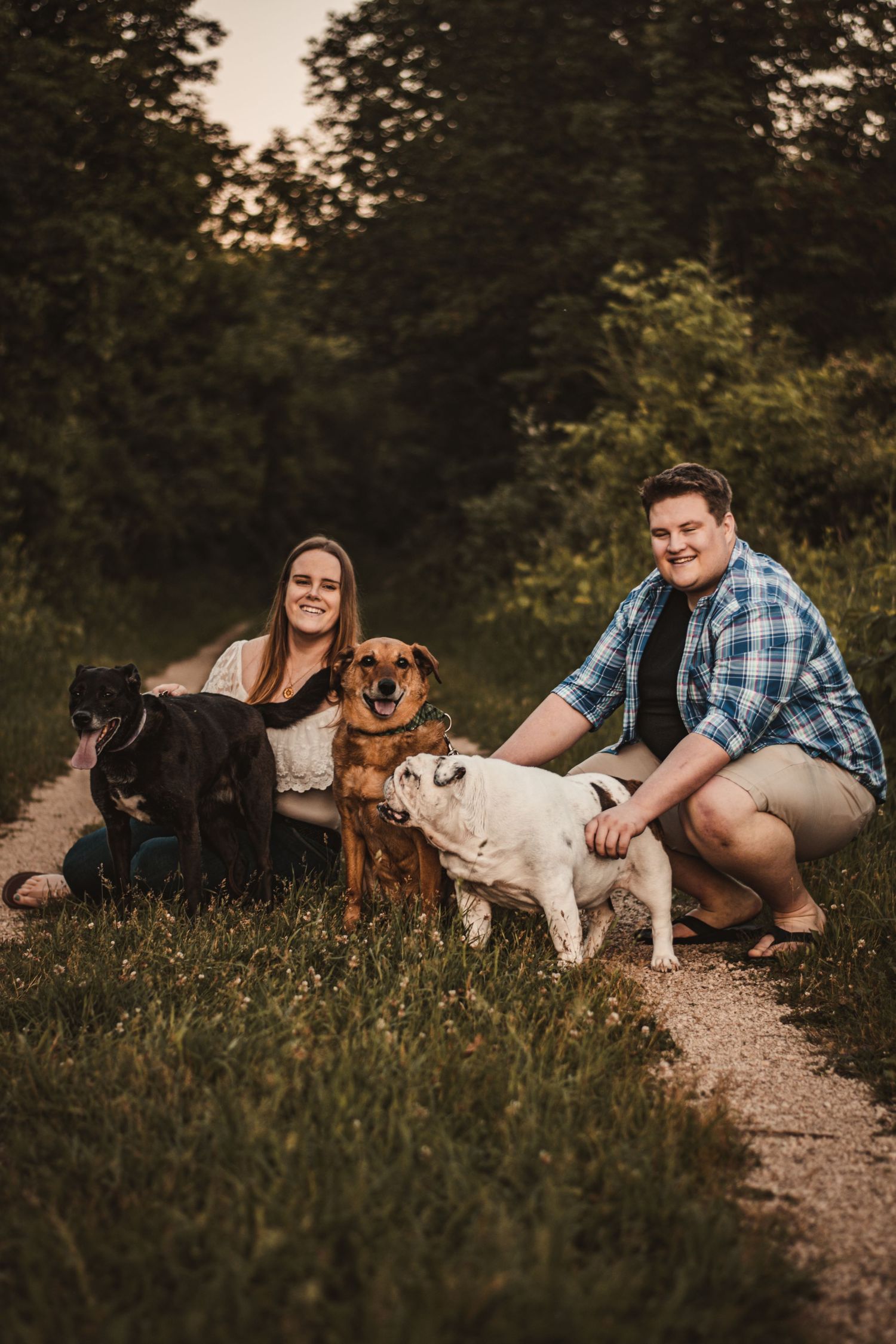 Happy couple posing with their three dogs on a nature trail at sunset.