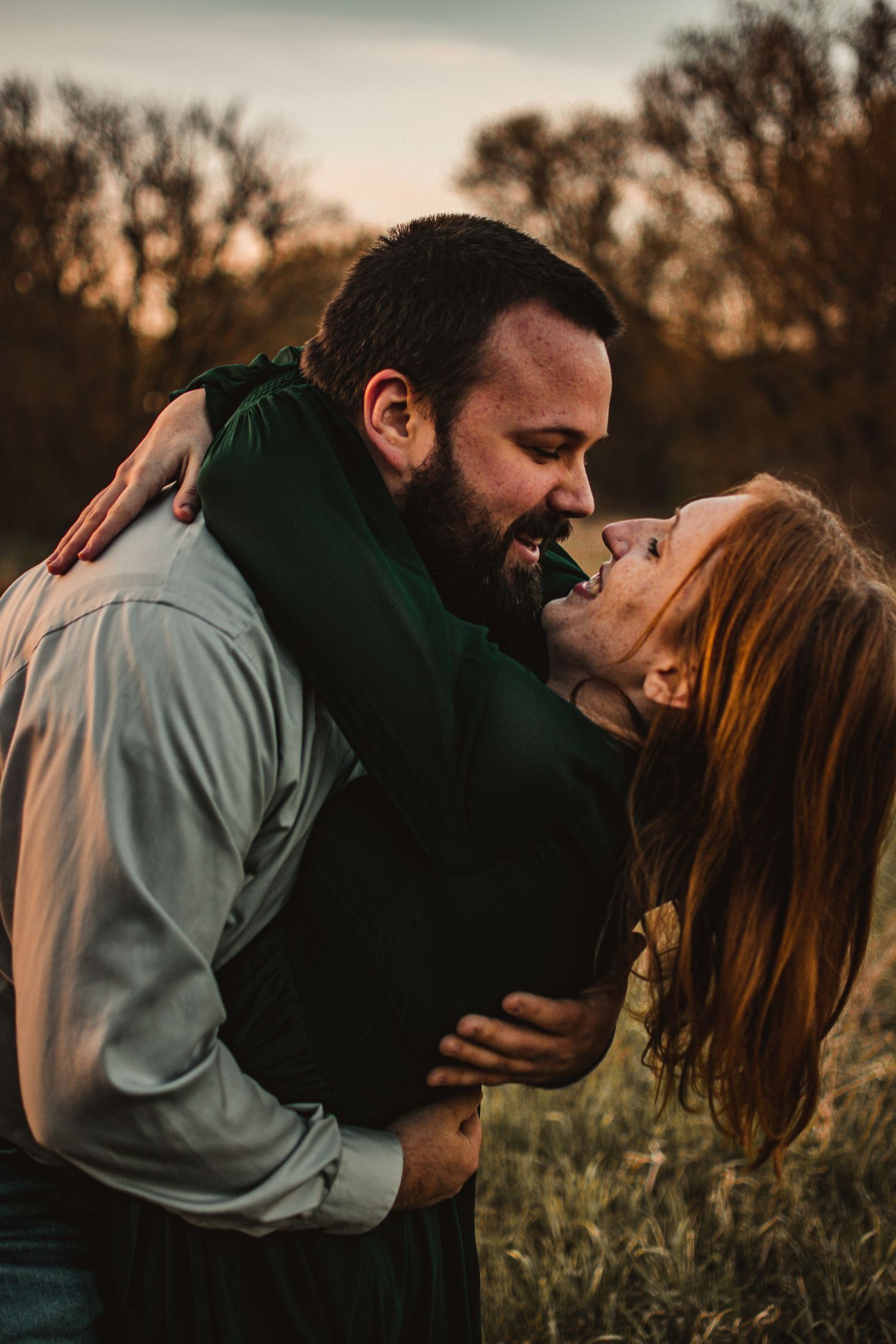 Couple sharing a joyful embrace at sunset in a field with golden lighting.