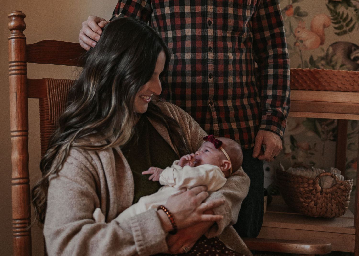 A new family sits together in a cozy nursery/baby's bedroom with a baby, sharing an intimate moment in warm lighting.