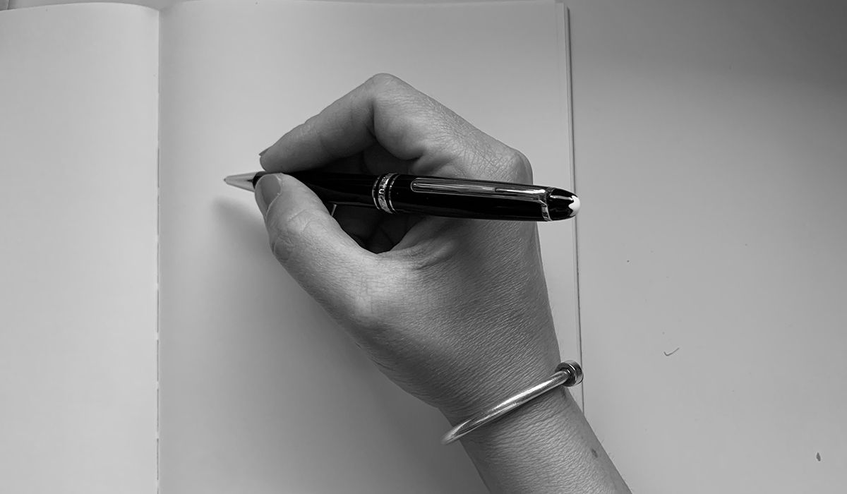 Eine Hand hält einen Stift über einem leeren Blatt Papier
